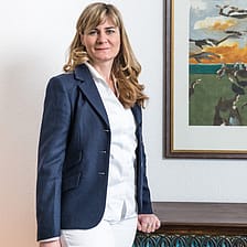 Paartherapeutin Vera Matt traegt blauen Blazer und steht in einem Zimmer vor einem Gemaelde