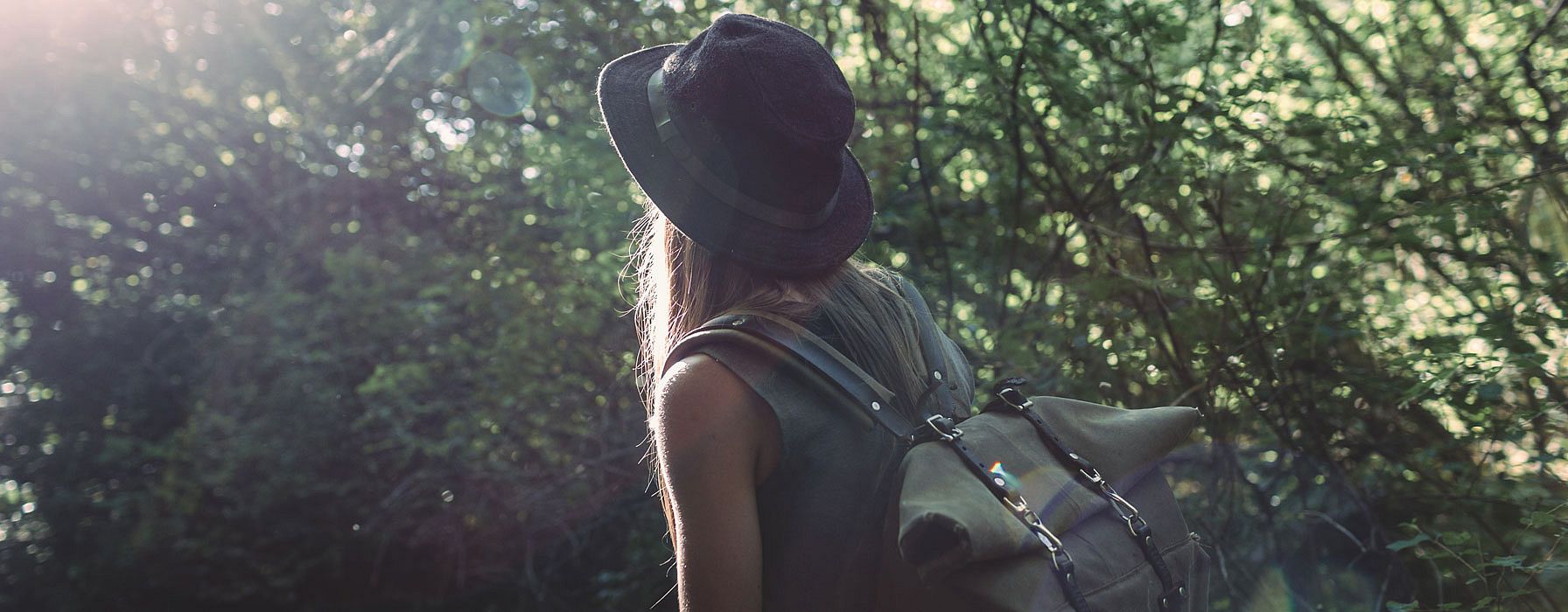 Frau mit Rucksack wandert am Waldrand entlang