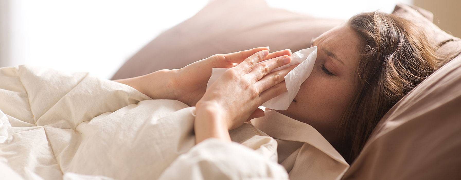 Frau im Bett schneuzt sich die Nase
