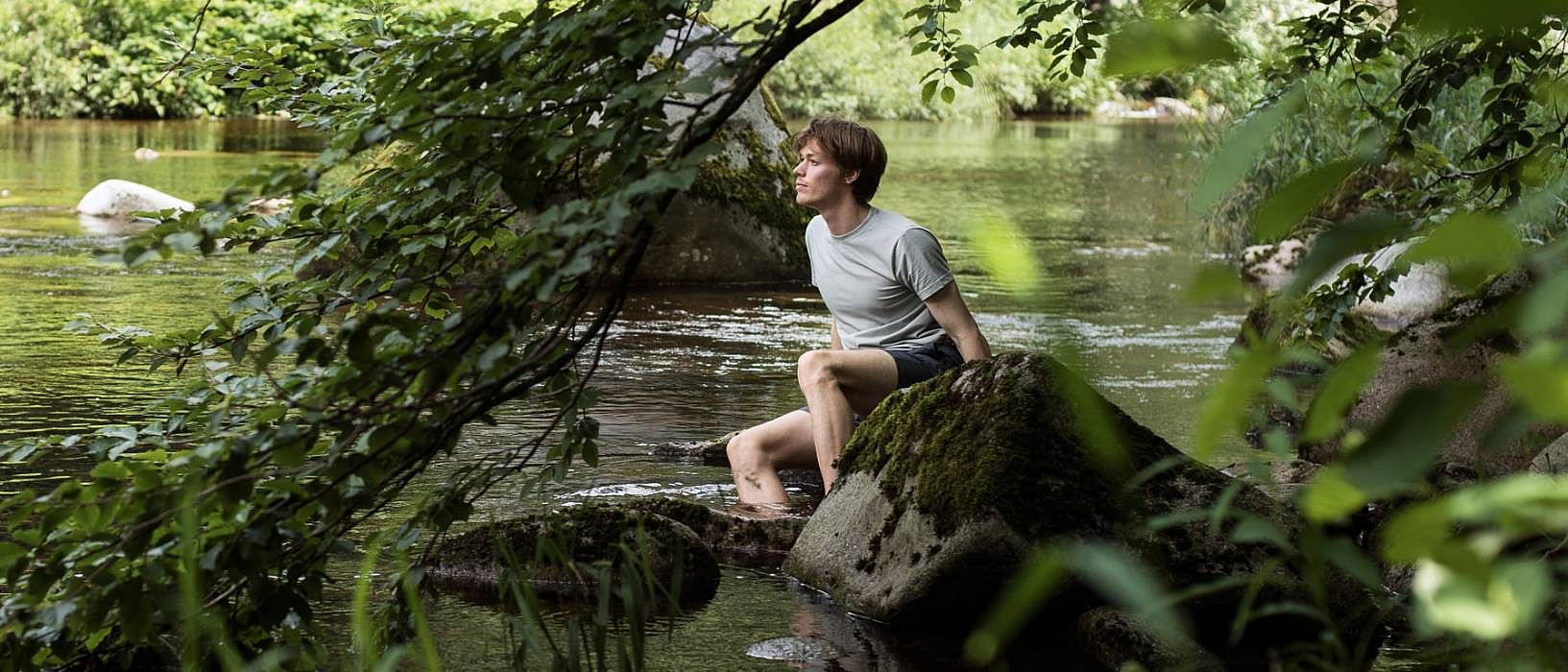 Mann sitzt auf einem Stein im See