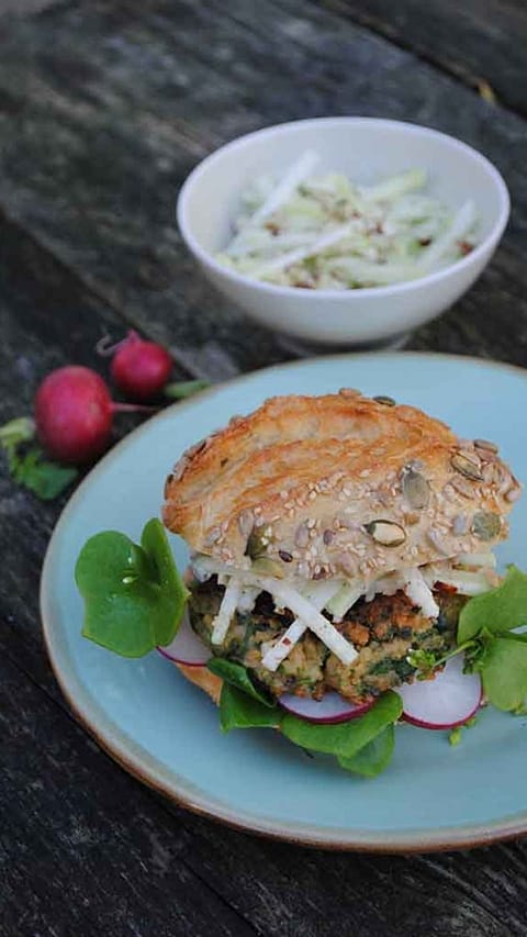 Der fertige Burger mit Salatblatt und Radieschen liegt angerichtet auf einem Teller