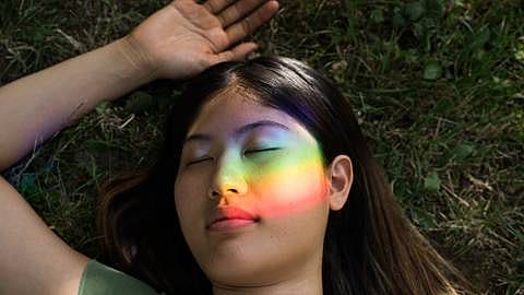 Frau mit geschlossenen Augen, im Gesicht die Spiegelung eines Regenbogenprismas