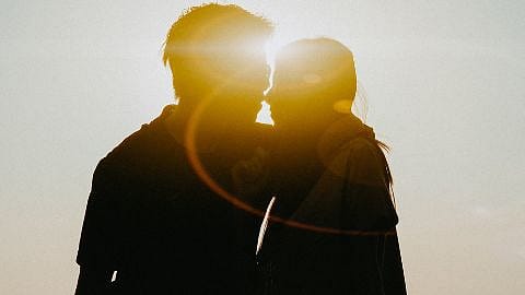 Ein Mann und eine Frau kuessen sich im Gegenlicht