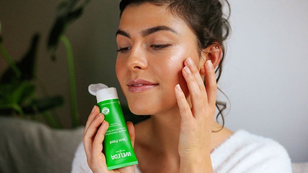 Alt text * Frau trägt Weleda Skin Food als Highlighter auf Wangenknochen auf