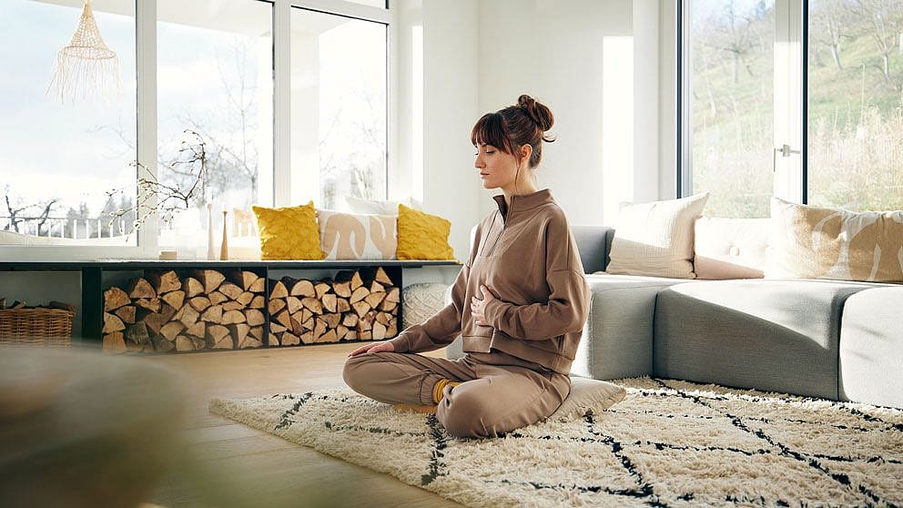 Frau im Yogasitz haelt sich den Bauch