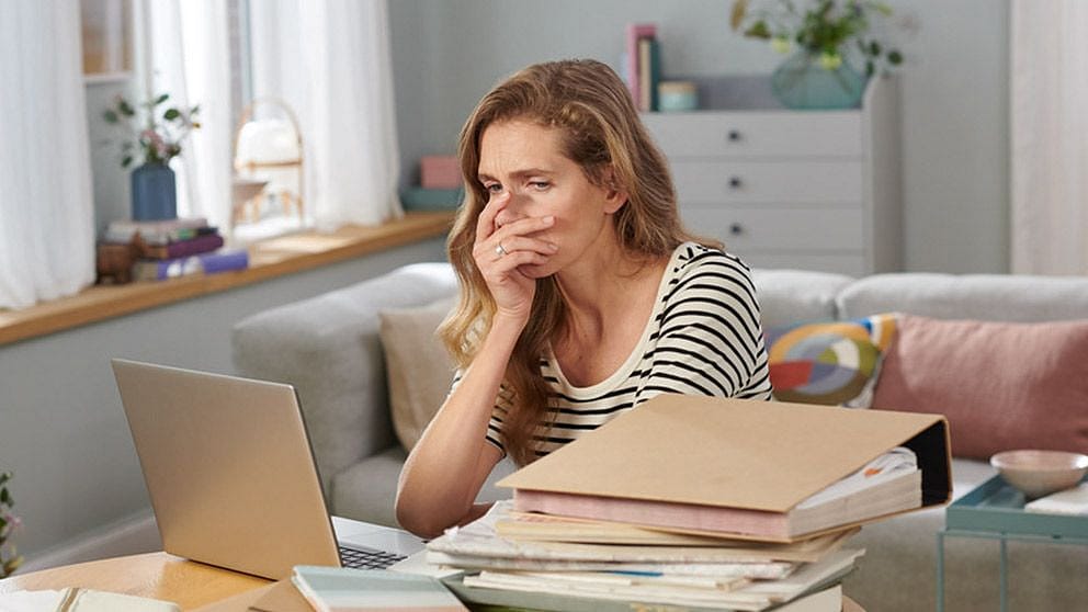 Verzweifelte Frau mit vielen Unterlagen vor dem Laptop