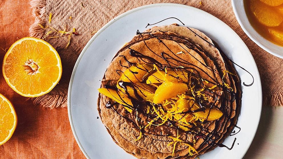Mehrere Kakao-Crêpes auf einem Teller garniert mit marinierten Orangen und Schokoladensauce